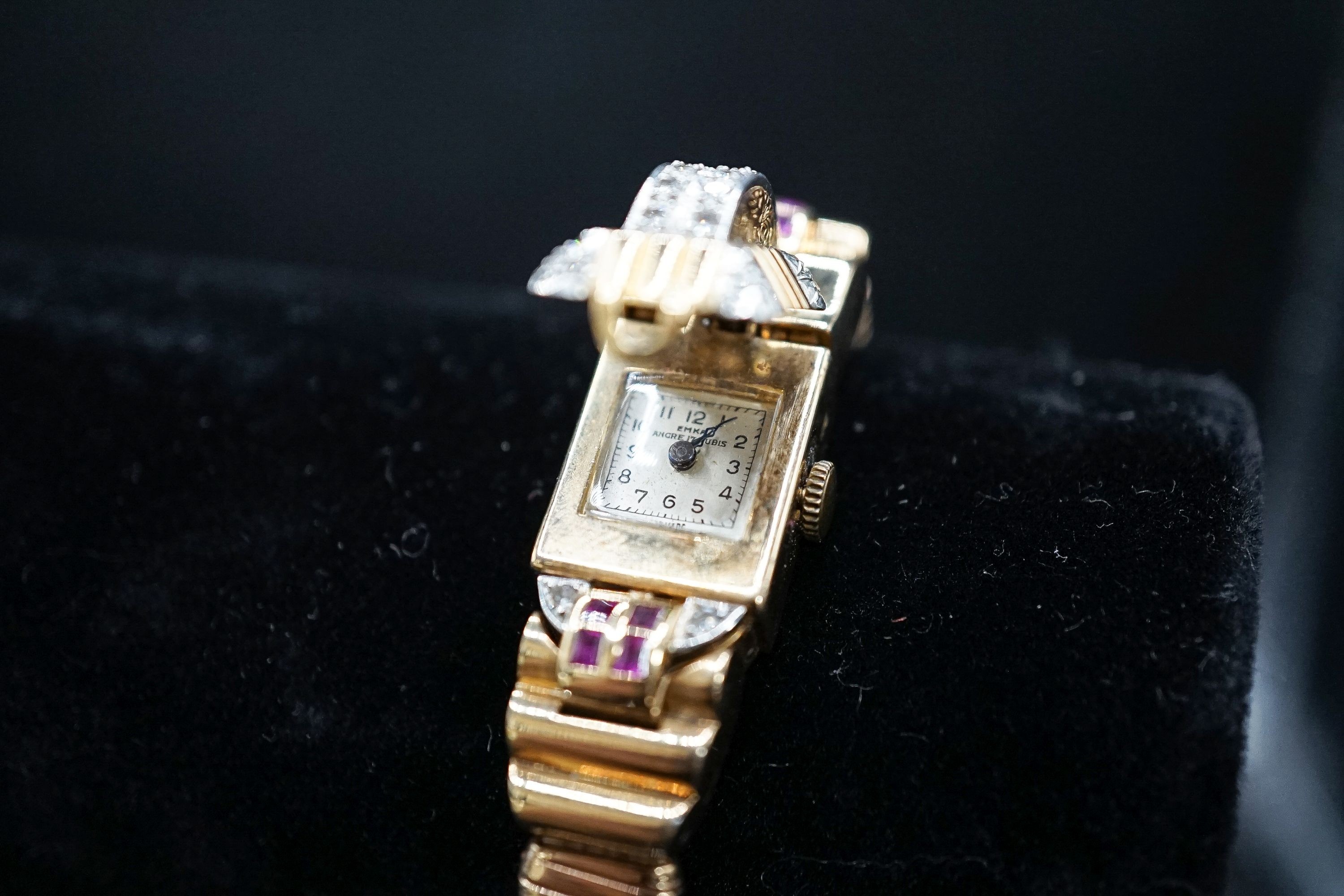 A 1950's 9ct gold, ruby and diamond set Emka manual wind cocktail watch, the dial with gem set hinged cover, gross weight 37.2 grams.